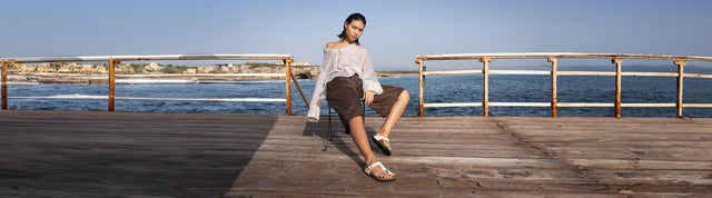 donna seduta su una sedia sul portico in riva al mare che indossa infradito birkenstock gizeh nubuck leather ecru